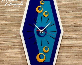 Puede incluir: Un reloj azul y turquesa con marco blanco y círculos amarillos. El reloj tiene agujas de hora y minuto negras y una aguja de segundo roja.