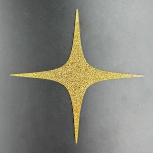 Puede incluir: Una forma de estrella dorada con purpurina y cuatro puntas. La estrella está centrada en un fondo gris oscuro. La estrella es un elemento decorativo.