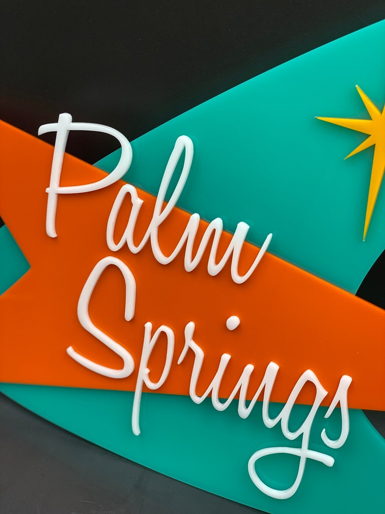 K&ouml;nnte beinhalten: Ein t&uuml;rkisfarbenes und orangefarbenes Schild mit wei&szlig;er Aufschrift "Palm Springs". Ein gelber Stern befindet sich in der oberen rechten Ecke des Schildes.