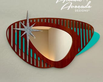 May include: A mid-century modern style wall mirror with a wood frame and a turquoise accent. The mirror has a unique shape and a starburst design.