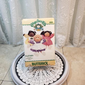 May include: A vintage Butterick sewing pattern for Cabbage Patch Kids clothing. The pattern features illustrations of the dolls in various outfits. The packaging is cream-coloured with the Cabbage Patch Kids logo and the number 6509.