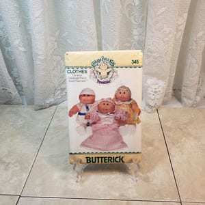 May include: A vintage Cabbage Patch Kids Preemie doll clothing pattern by Butterick. The pattern is number 345 and features three dolls wearing different outfits. The pattern is on a white background with green and red text.