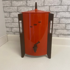 May include: A vintage orange and brown coffee carafe with a spigot and three crown-shaped designs on the front.
