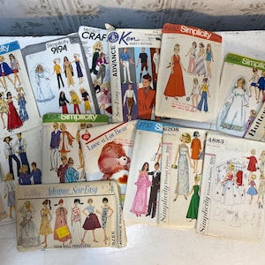 May include: A collection of vintage sewing patterns featuring illustrations of dolls and fashion designs. Brands include Simplicity, Butterick, and Advance. The patterns showcase various styles, including dresses, suits, and bridal wear, with text such as "Teen Doll Trousseau."