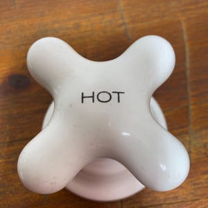 May include: White ceramic hot water faucet handle with a four-point star shape and the word "HOT" printed in black.