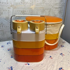 May include: Vintage retro-style cooler and beverage dispenser set. The cooler is white, yellow, orange, and has a handle. The beverage dispenser is yellow, white, and orange with two spouts. Both items have orange lids.