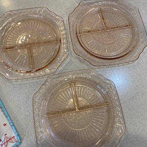May include: Three pink glass divided serving plates with a scalloped edge and a sunburst pattern.