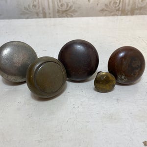 May include: A collection of antique door knobs in various sizes and finishes. The knobs range in color from tarnished silver to dark brown and brass. The shapes are primarily spherical.