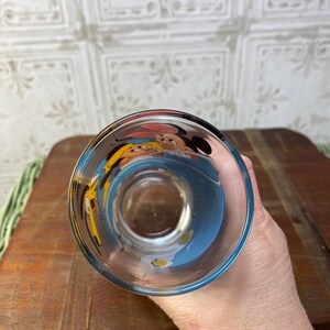 May include: A clear glass with a blue, yellow, and white design featuring Mickey Mouse and Minnie Mouse. The glass is upside down.
