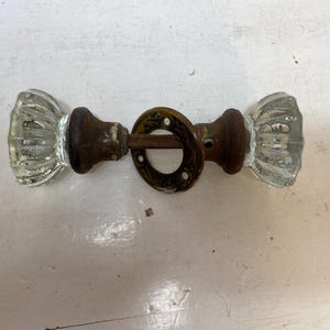 May include: Antique glass door knobs with a ribbed design and brass hardware. The knobs are clear and the hardware is aged with a vintage look. A classic hardware piece for doors.