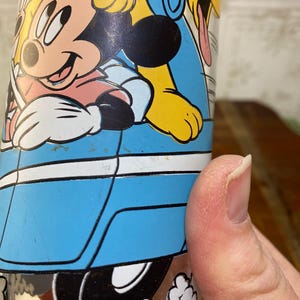 May include: A blue glass cup with a cartoon image of Mickey Mouse, Pluto, and Donald Duck. The characters are in a blue car with white trim. The car is driving on a white road with white clouds.
