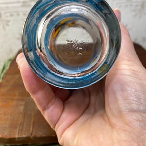 May include: The bottom of a clear glass drinking glass with a blue rim. The glass has a small, faded mark on the bottom.