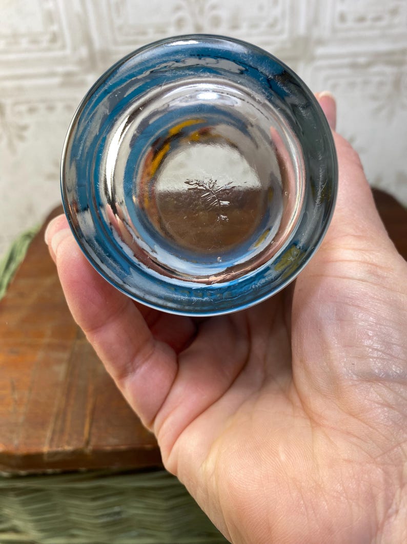 May include: The bottom of a clear glass drinking glass with a blue rim. The glass has a small, faded mark on the bottom.