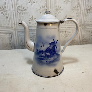 May include: Vintage white and blue enamelware coffee pot. The pot features a windmill and house scene in blue. The pot has a curved spout, a handle, and a lid. The pot is approximately 10 inches tall.