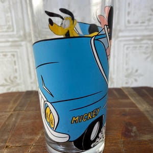 May include: A blue glass with a cartoon image of Mickey Mouse, Pluto, and Goofy driving a blue car. The car has the word "MICKEY" printed on the side.