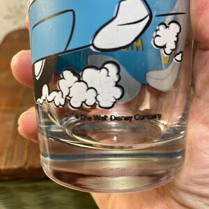 May include: A clear glass drinking glass with a blue and white cartoon image of a car with smoke coming out of the exhaust. The text "The Walt Disney Company" is printed on the bottom of the glass.