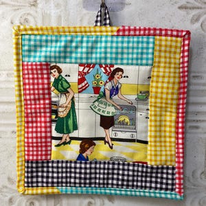 May include: A colourful quilted hot pad featuring a vintage kitchen scene with three women in a kitchen. The hot pad is made from different coloured gingham fabrics in red, yellow, blue and black.
