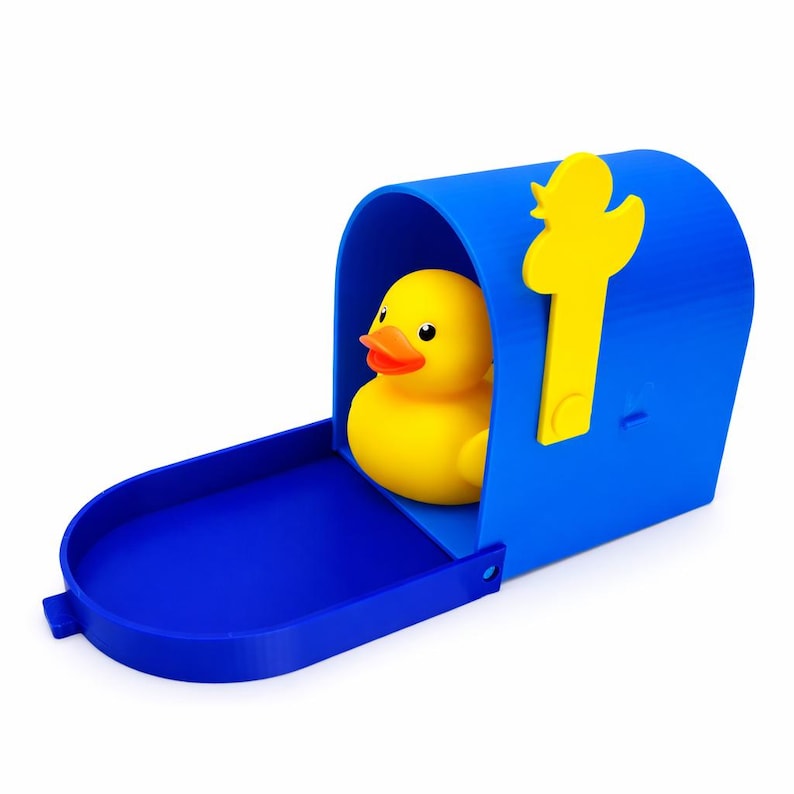 Puede incluir: Un patito de goma amarillo dentro de un buz&oacute;n azul con una bandera amarilla. El buz&oacute;n tiene una bandeja abierta. El pato tiene un pico naranja.
