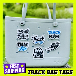 May include: A light blue tote bag with various track and field themed stickers. The stickers include the text "Track Mom", "Track Life", "That's my Grandson out there", "Track", and "1234 Track".