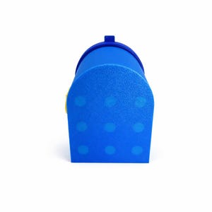 Puede incluir: Un buz&oacute;n azul con una parte superior redondeada y una peque&ntilde;a bandera rectangular. El buz&oacute;n tiene una superficie texturizada y est&aacute; decorado con lunares azul claro. Un acento amarillo es visible en el lateral.
