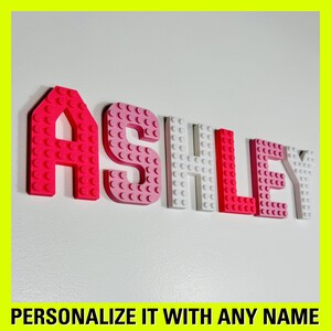 May include: The name "ASHLEY" is spelled out in pink, white, and red plastic letters that resemble Lego bricks.  Personalize it with any name.