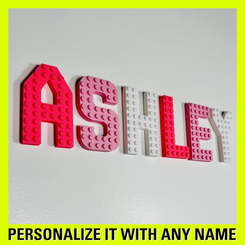 May include: The name "ASHLEY" is spelled out in pink, white, and red plastic letters that resemble Lego bricks.  Personalize it with any name.