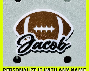 Puede incluir: Un balón de fútbol blanco y marrón con el nombre "Jacob" en blanco y negro. El balón está sobre un fondo gris.