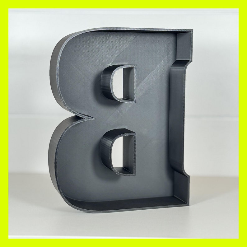 May include: A black, three-dimensional letter B. The letter is made of a solid material and has a hollow center.