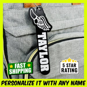 May include: Black and white personalized luggage tag with a running shoe and wing design. The tag says "TAYLOR" in white letters. The tag is attached to a gray backpack. The image also includes a 5 star rating sticker.