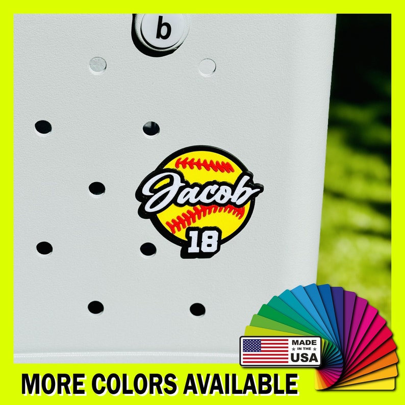 May include: A white softball with red stitching and the name "Jacob" and the number "18" in black. The softball is on a white surface with a black background. The text "MADE IN THE USA" is in the lower right corner of the image.