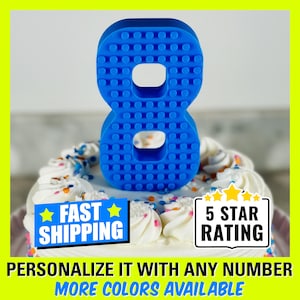 May include: Blue plastic number eight cake topper shaped like Lego bricks. The topper is on a white cake with colorful sprinkles. The text "Fast Shipping" and "5 Star Rating" are on the image.