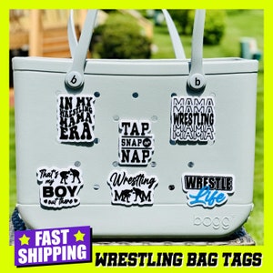 May include: A light blue tote bag with various wrestling-themed stickers. The stickers feature phrases like "In My Wrestling Mama Era", "Tap Snap or Nap", "Wrestling Mom", "That's My Boy", "Wrestle Life", and "Mama Wrestling Mama".