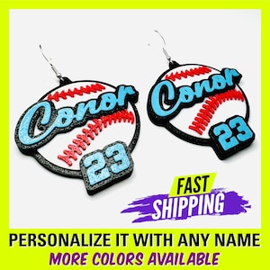 May include: A pair of personalized baseball earrings with the name "Conor" and the number "23" in blue. The earrings are made of black, white, red, and blue acrylic.