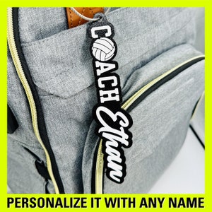 May include: A black and white volleyball coach keychain with the text "COACH Ethan" on a gray backpack.