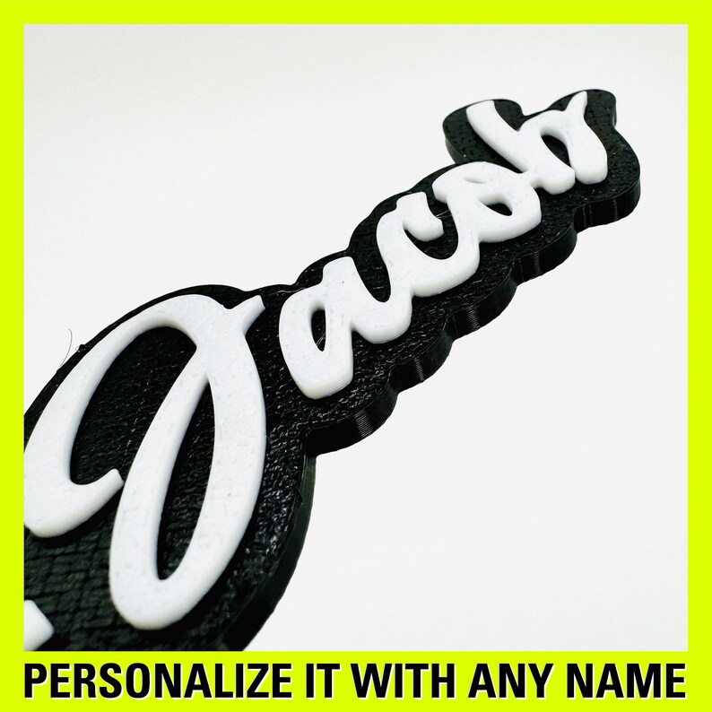 May include: A black and white 3D printed name sign with the name "Jacob" in a cursive font. The sign is made of a textured material and has a raised edge.