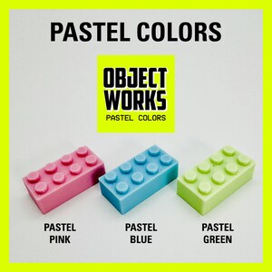 May include: Three pastel colored plastic toy building blocks. The blocks are pink, blue, and green. The blocks are arranged in a row from left to right. The text "OBJECT WORKS PASTEL COLORS" is visible above the blocks.