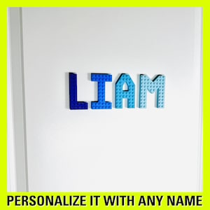 May include: A white door with the name "LIAM" spelled out in blue plastic letters. The letters are made of Lego bricks and are arranged in a straight line. The text "PERSONALIZE IT WITH ANY NAME" is at the bottom of the image.