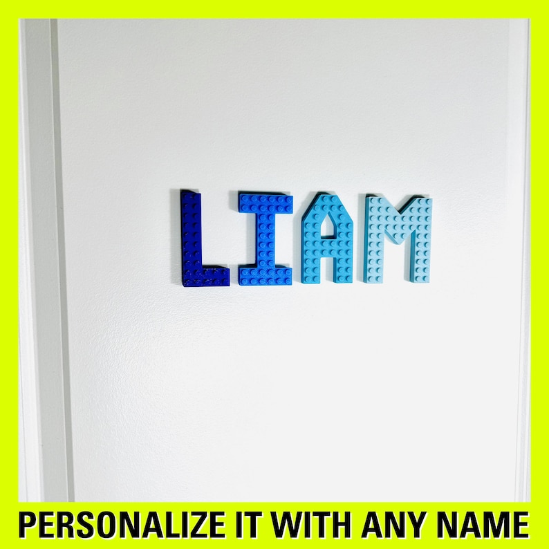 May include: A white door with the name "LIAM" spelled out in blue plastic letters. The letters are made of Lego bricks and are arranged in a straight line. The text "PERSONALIZE IT WITH ANY NAME" is at the bottom of the image.