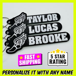 May include: Three black and white personalized keychains with a running shoe and wings design. The keychains are labeled "TAYLOR", "LUCAS", and "BROOKE".