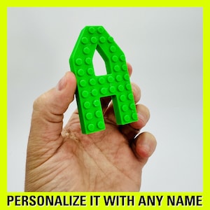 May include: A green plastic letter A made of small squares. The letter is being held in a hand.