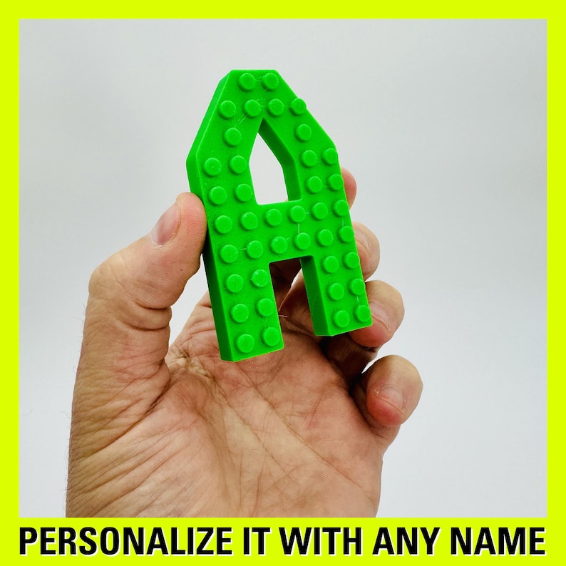 May include: A green plastic letter A made of small squares. The letter is being held in a hand.