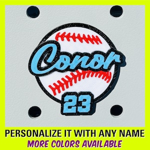 May include: A baseball-themed design featuring a baseball with red stitching, the name "Conor" in light blue, and the number "23" in a light blue font. The design is set against a white background with a black border. The text "PERSONALIZE IT WITH ANY NAME" and "MORE COLORS AVAILABLE" is at the bottom.