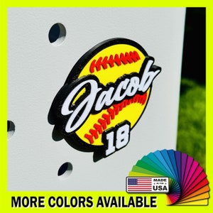 May include: A yellow and black softball with red stitching and the name "Jacob" and the number "18" on it. The softball is on a white background. Made in the USA.