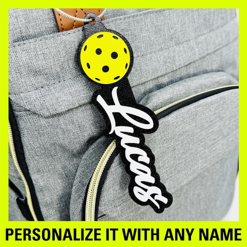 Peut inclure: Une &eacute;tiquette &agrave; bagages personnalis&eacute;e noire et blanche avec le mot "Lucas" &eacute;crit en cursive. L'&eacute;tiquette pr&eacute;sente un design de pickleball jaune et noir.