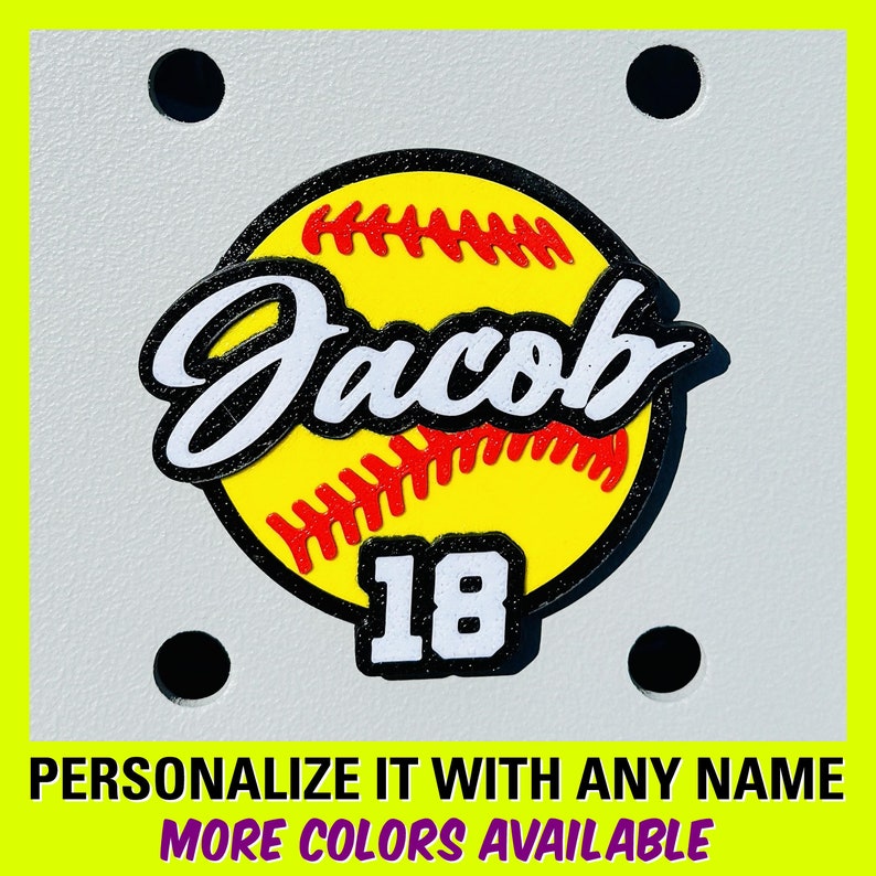 May include: A yellow softball with red stitching and a black outline. The name "Jacob" is written in a white cursive font on the softball. The number "18" is written in white on a black background below the softball.