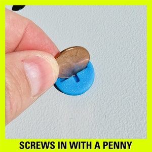 May include: A hand holding a penny over a blue, sparkly, round button with a cross-shaped hole in the centre. The caption below the image reads "Screws in with a penny".