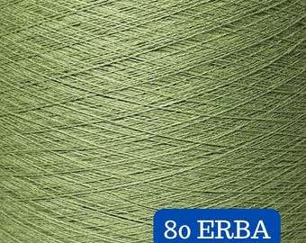May include: Close-up of a spool of olive green thread. The thread is tightly wound, creating a textured surface. A blue rectangular label at the bottom reads "80 ERBA" in white text. The thread appears to be for sewing or crafting.