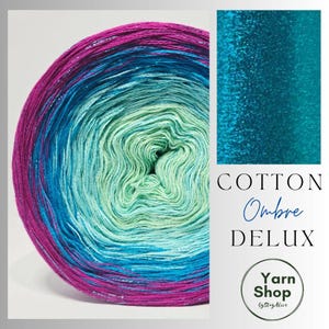 Puede incluir: Una vibrante madeja de hilo ombre en tonos fucsia, turquesa y verde menta. El hilo está etiquetado como "Cotton Ombre DELUX" y es de Yarn Shop by StayAlive.