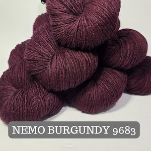 Könnte beinhalten: Mehrere Stränge burgunderfarbener Wolle. Die Wolle hat eine sichtbare Textur und einen tiefen, satten Farbton. Der Text "NEMO BURGUNDY 9683" wird in einem grauen Feld am unteren Bildrand angezeigt.
