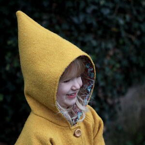 May include: A child wearing a yellow hooded coat with a floral lining. The hood is pointed and the coat has a button closure.